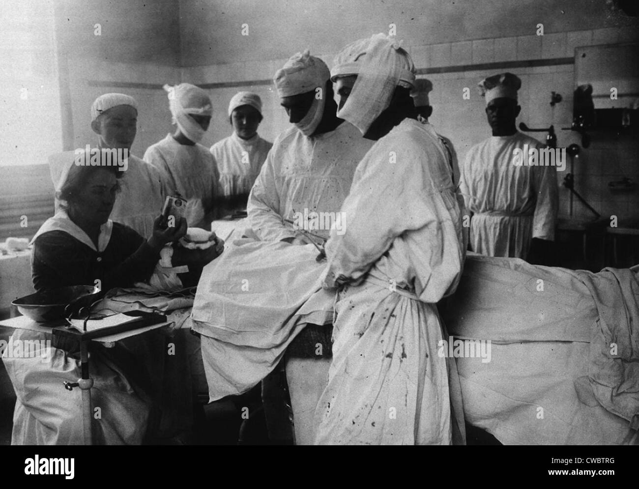 Masked surgeons perform an operation while a nurse administers ether to ...