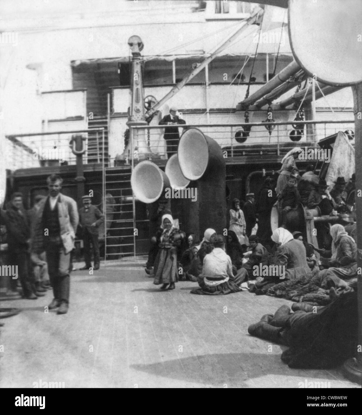 Steerage passengers taking life easy on an ocean liner. Immigrants relax and stroll on the open deck amidst ventilation Stock Photo