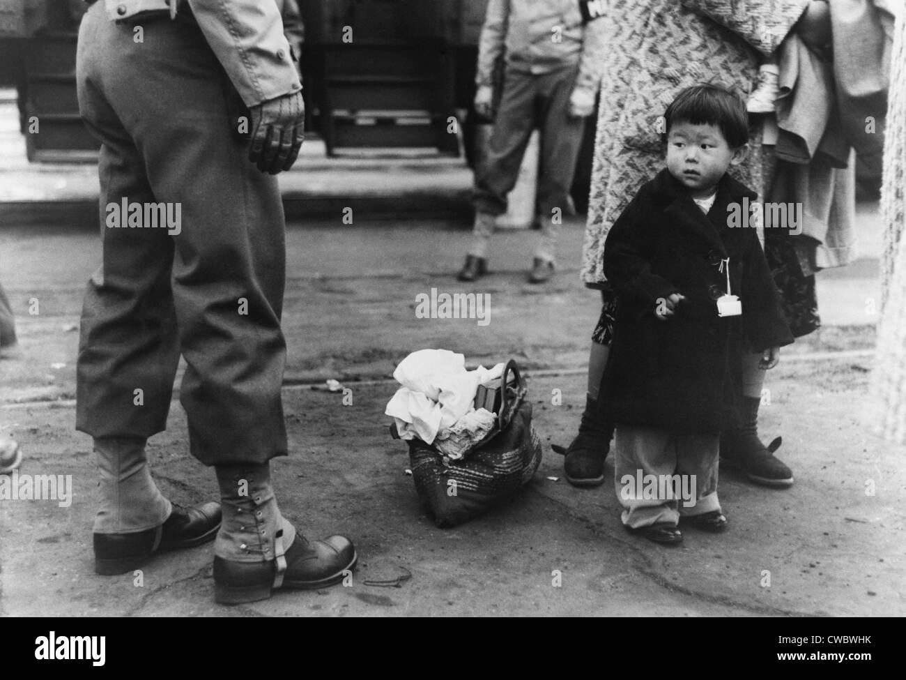 Small child looks apprehensively at the U.S. soldier supervising the transport of Los Angeles Japanese-Americans to Owens Stock Photo