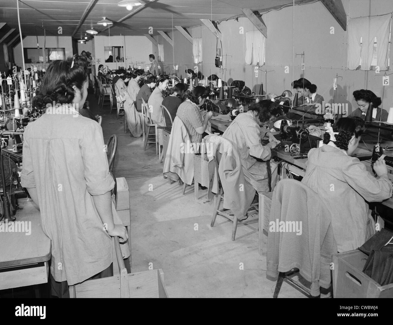 Interned Japanese American, Sumiko Shigematsu, standing at left, supervises fellow internees working at sewing machines at Stock Photo