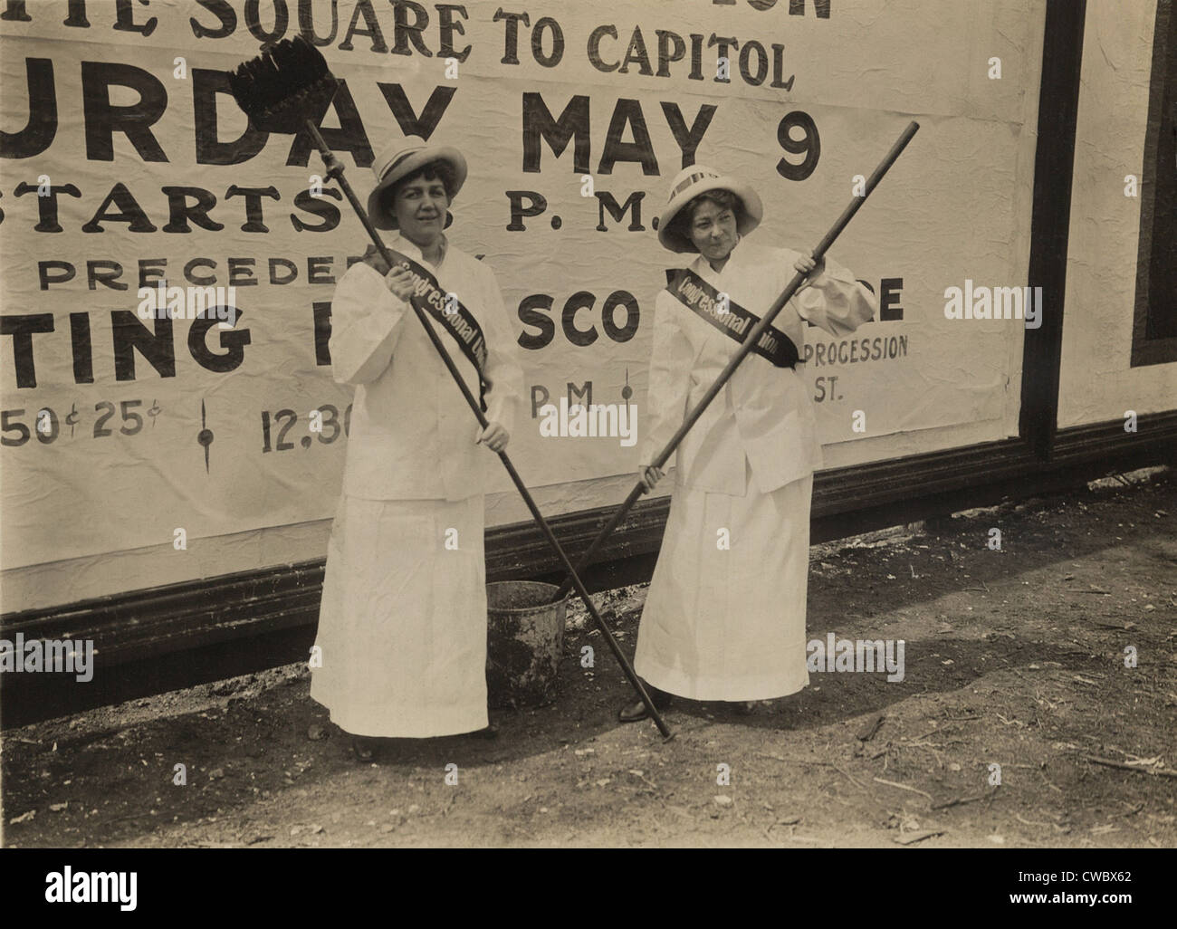 Two members of the Congressional Union for Woman Suffrage holding brushes in front of a large billboard advertisement for the Stock Photo