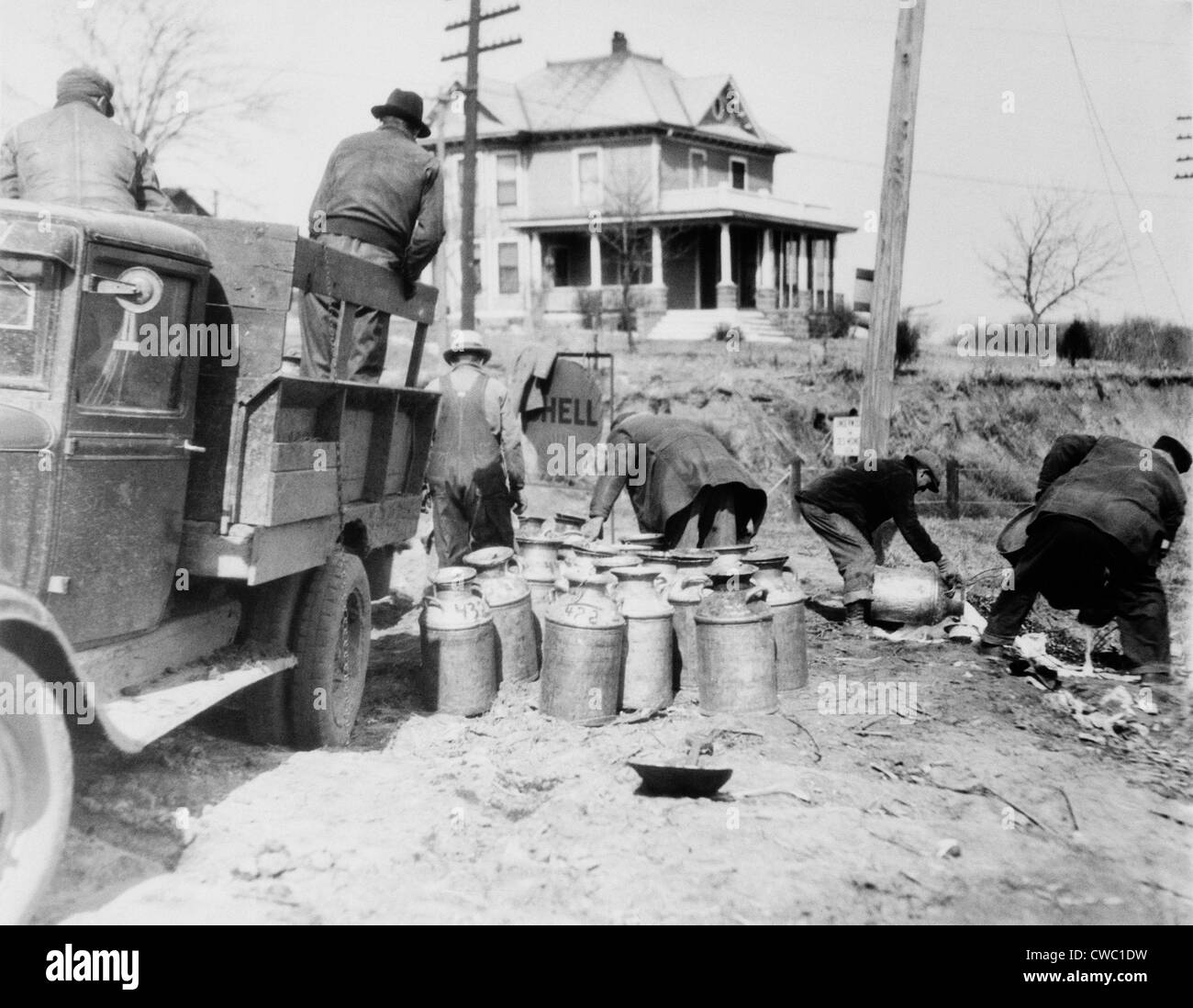 Striking farmers dump milk cans from a truck they have stopped to prevent delivery to market during the Great Depression. Milk Stock Photo