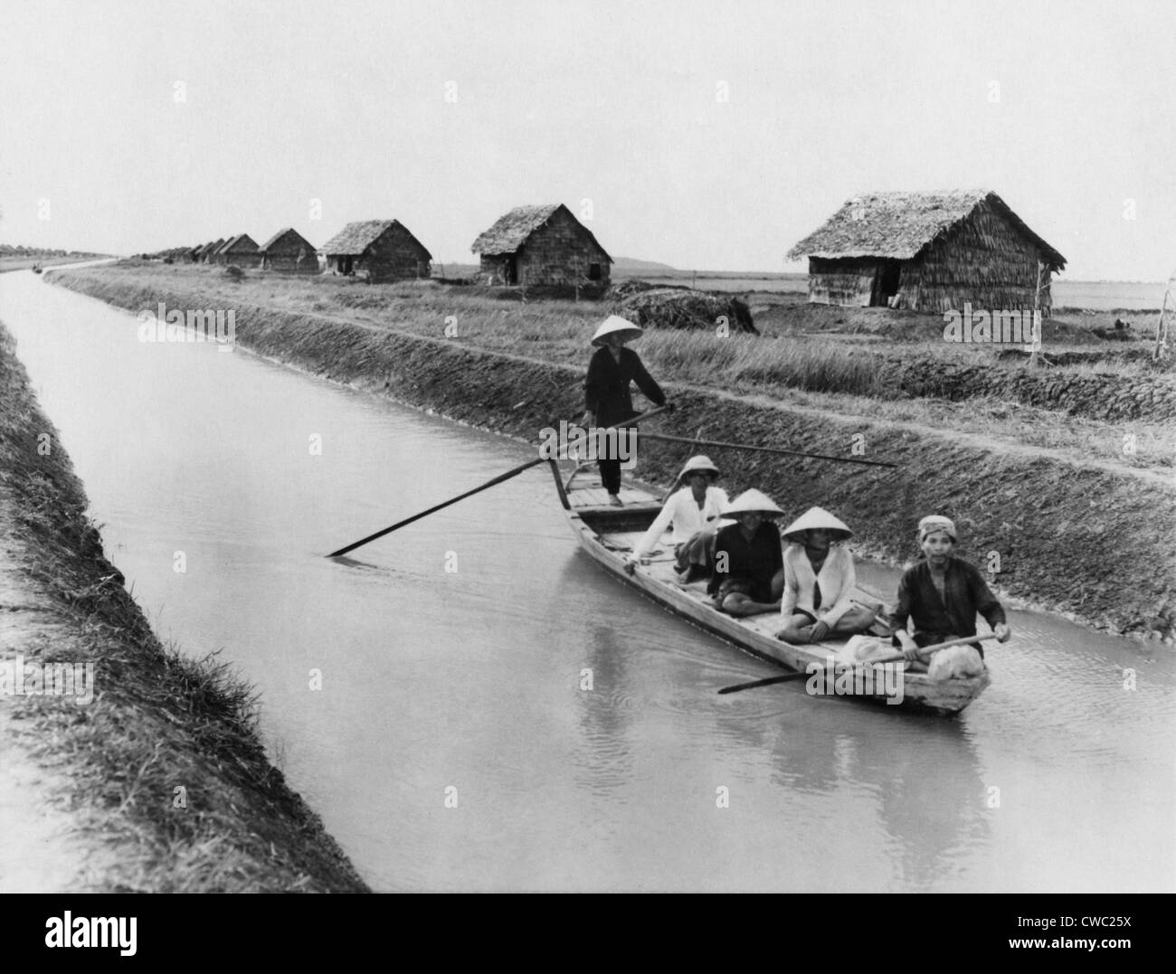 Vietnamese men in a sampan on a canal near straw dwellings that house refugees from North Vietnam. 1956. LC-DIG-ppmsca-09168 Stock Photo