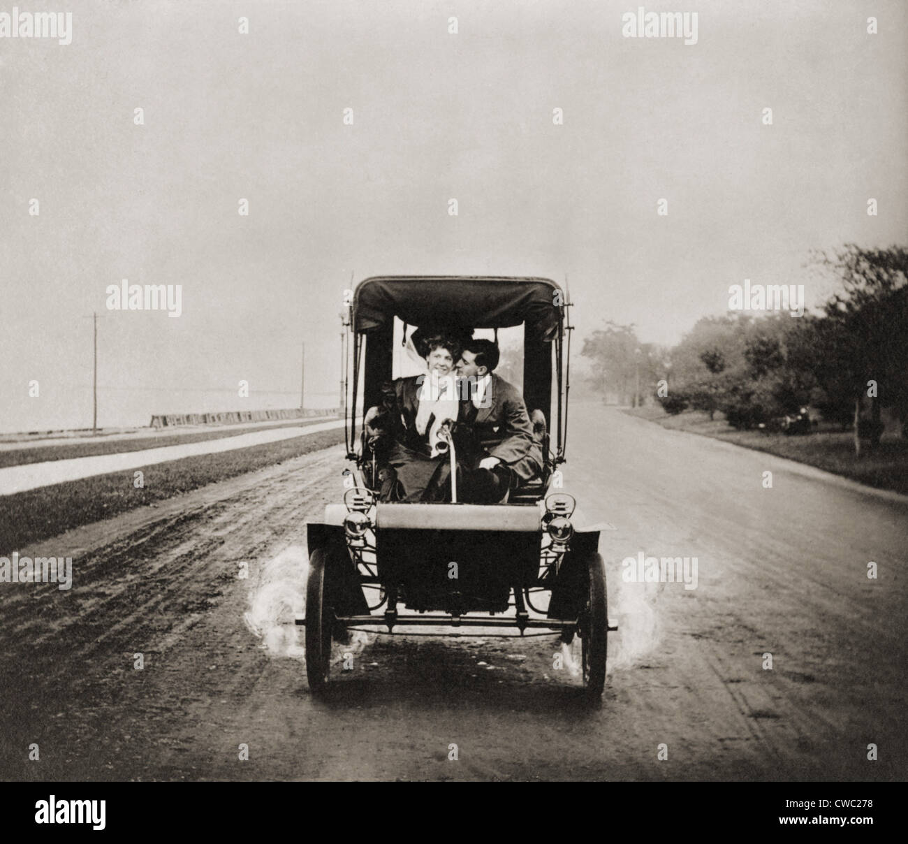 HE LETS HER STEER WHILE HE GETS HER EAR. Affectionate young couple enjoying the privacy of an automobile in 1907 LC-USZ62-111679 Stock Photo