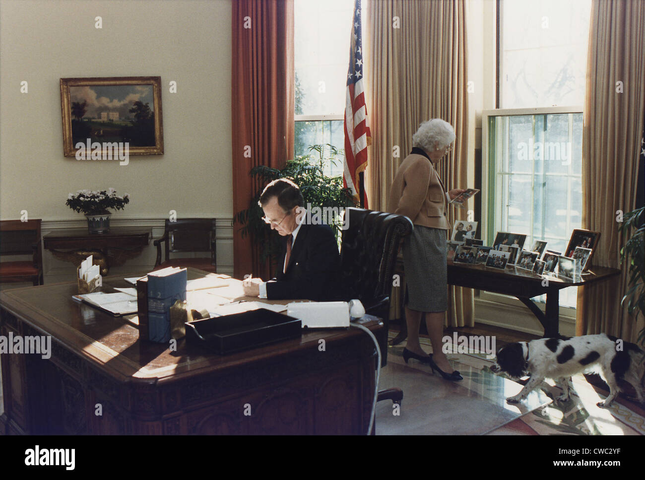 During his first week as president George Bush works in the Oval Office as wife Barbara looks at photographs behind the his Stock Photo