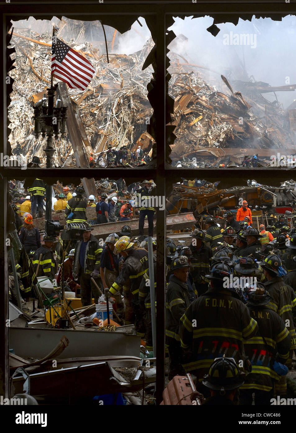 Seen through a broken window New York City firemen and rescue workers work their way toward the pile of burning ruins of the Stock Photo