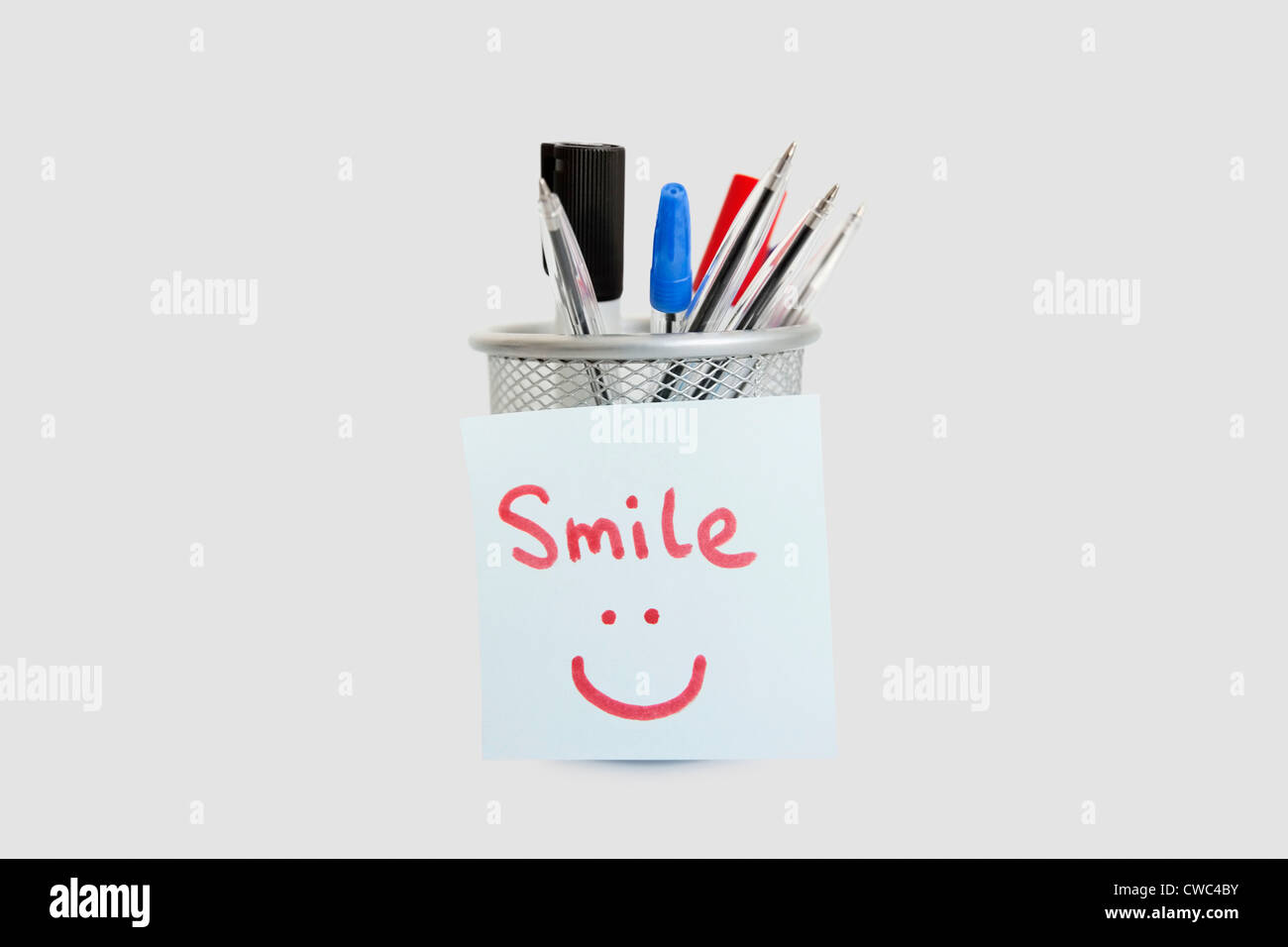 Close-up of adhesive notepaper with smiley face stuck on pen holder over white background Stock Photo