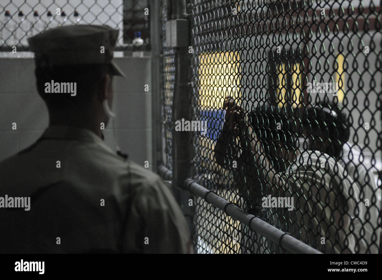 U.S. Sailor stands watch over a cell block at U.S. Naval Station Guantanamo Bay military prison while detainees look through Stock Photo