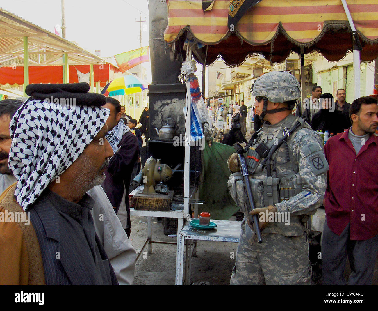 US soldier patrols the streets of Martyrs Market as local nationals shop in Mahmudiyah Iraq a Sunni Iraqi city south of Baghdad Stock Photo