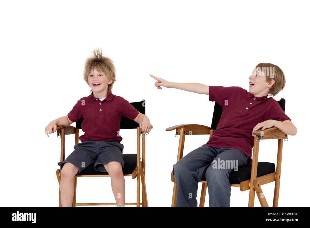 Pre-teen boy pointing at friend's hair while sitting on director's chair over white background Stock Photo