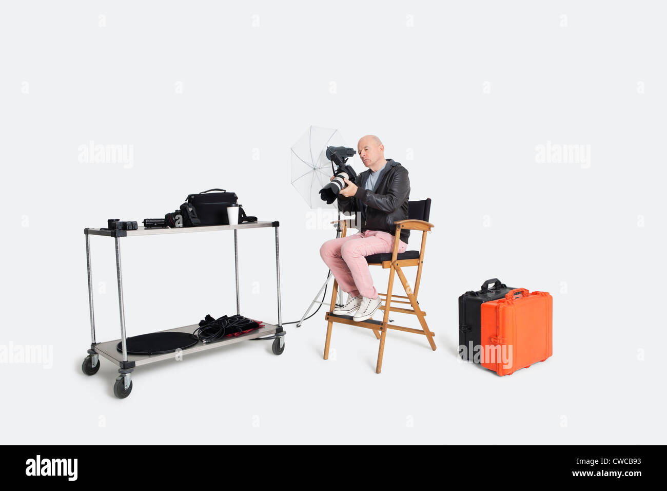 Senior photographer looking at camera while sitting on director's chair in studio Stock Photo