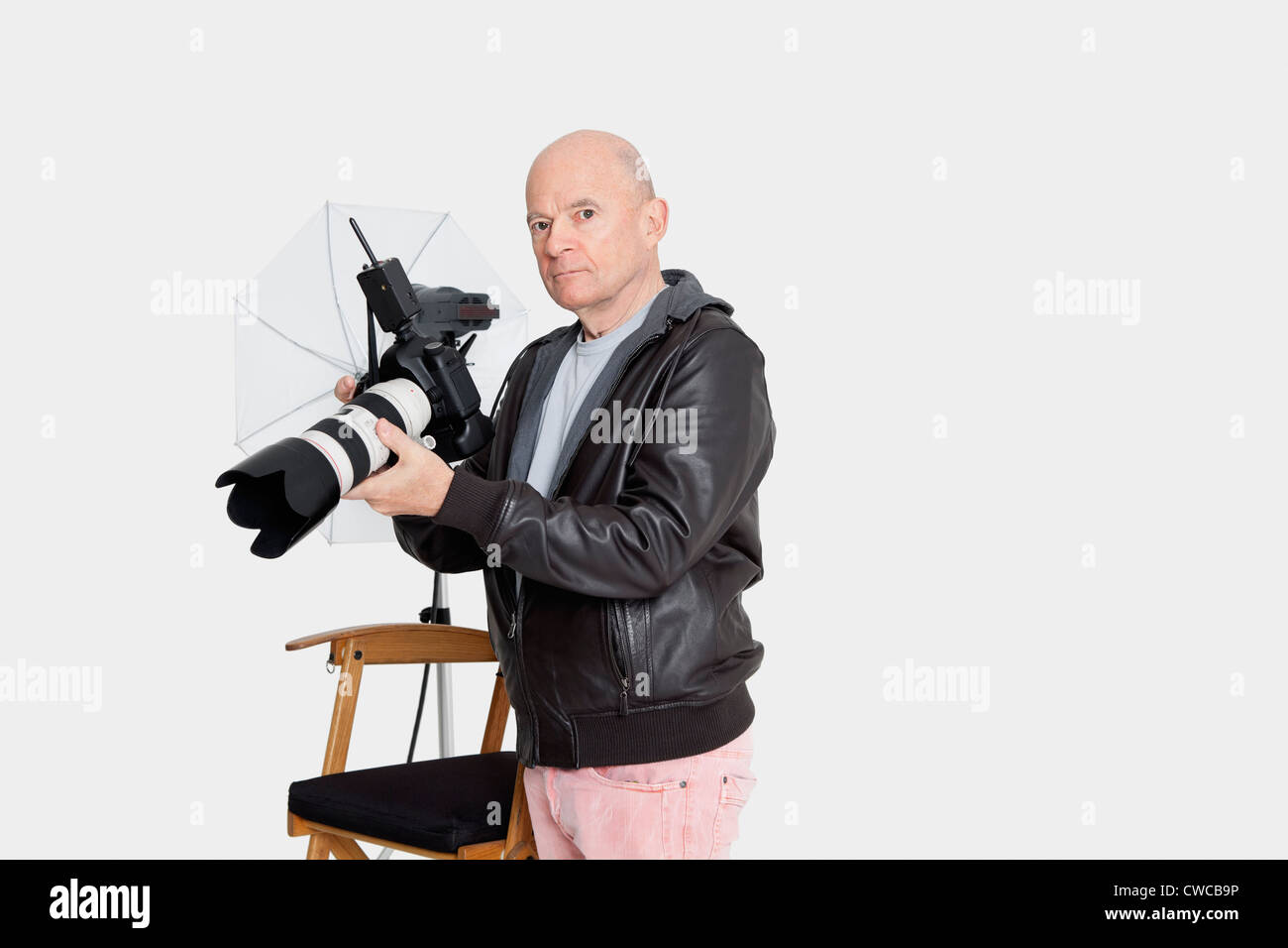 Senior photographer holding camera standing in studio Stock Photo