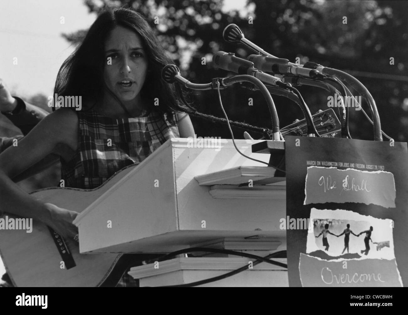 Folk Singer Joan Baez singing at the 1963 Civil Rights March on Washington. A sign hanging near the microphones reads 'We Shall Stock Photo