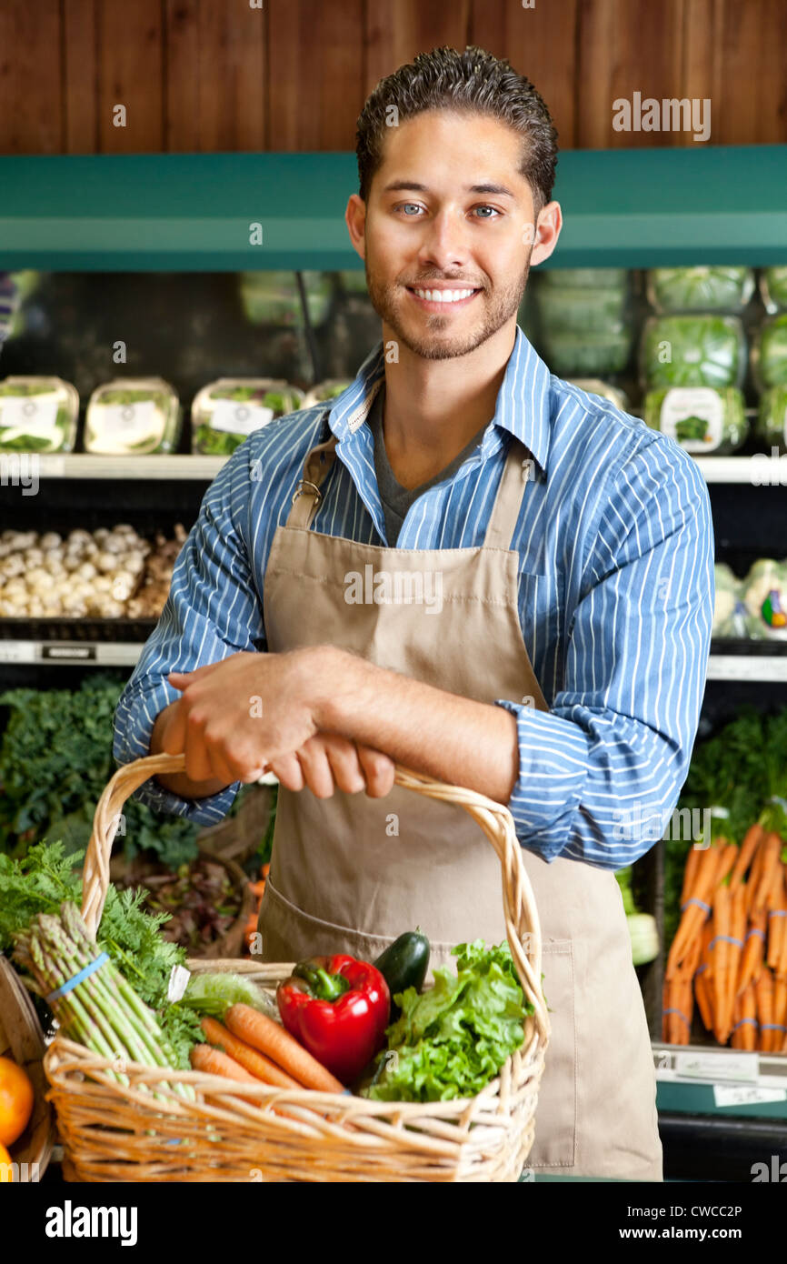 Portrait of handsome young salesperson standing with basket full of vegetables Stock Photo