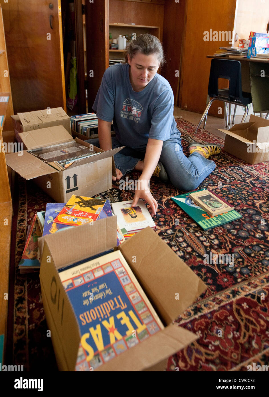 White female volunteer helps organize books to be used in classroom of elementary school in Austin, Texas Stock Photo