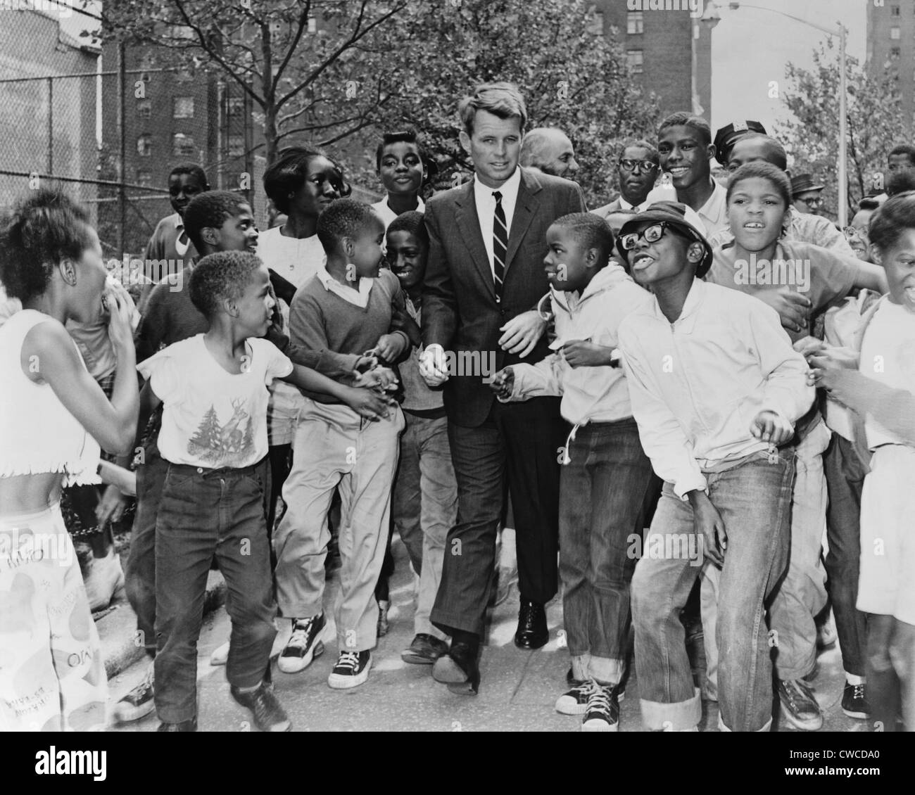 Attorney General Robert Kennedy surrounded by African American children. He was visiting a summer reading program in Harlem at Stock Photo