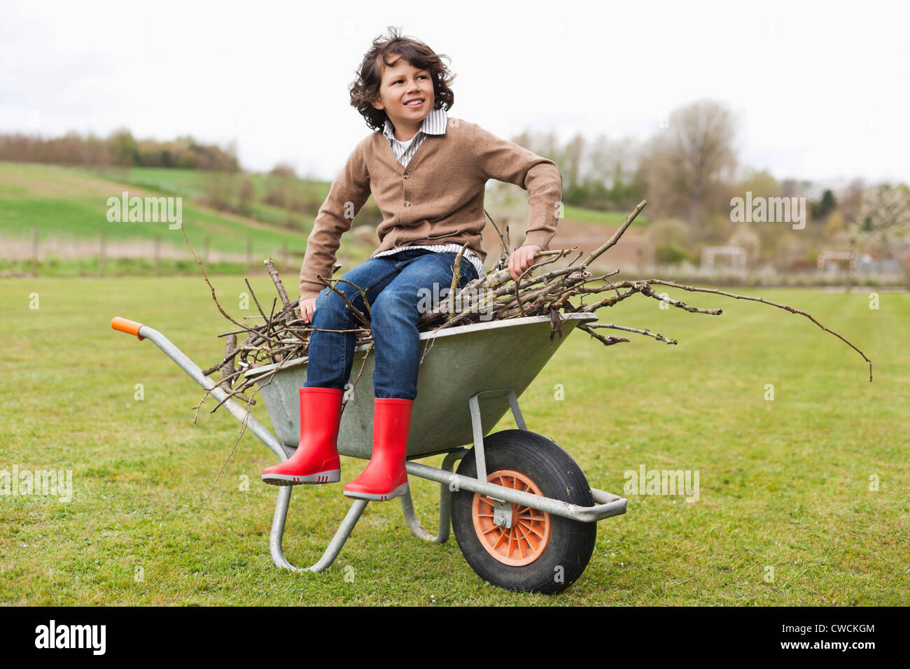 Boy sitting on a wheelbarrow with firewood in a field Stock Photo - Alamy