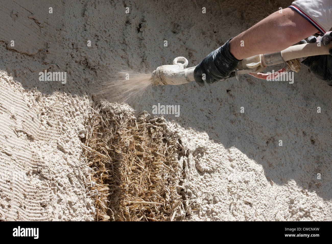 Render being applied to a straw covered building Stock Photo
