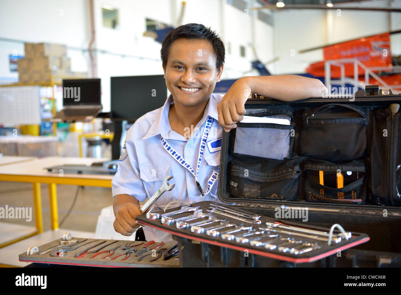 Helicopter engineer standing next to tool box is smiling and holding a wrench. Stock Photo
