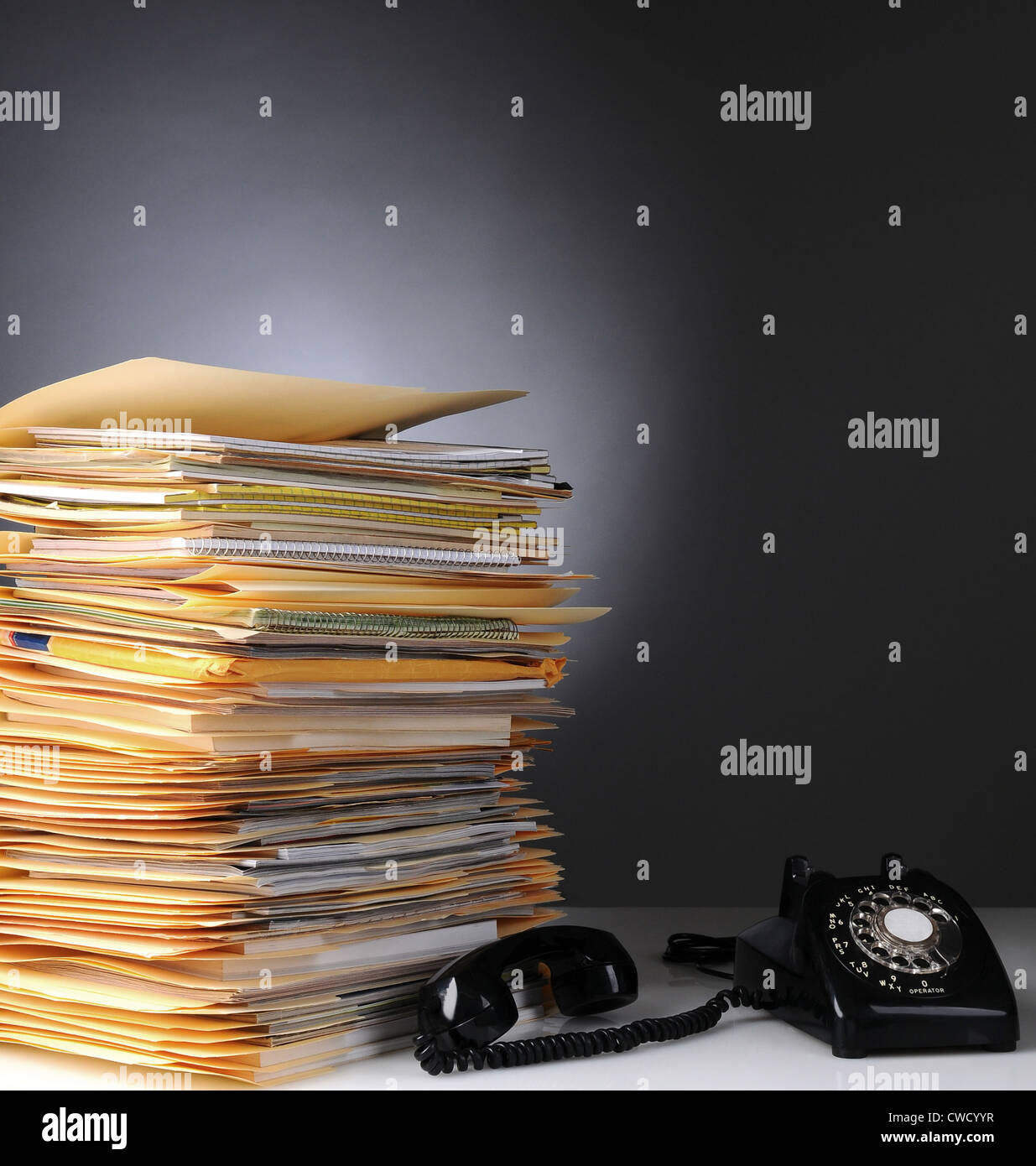 A large stack of files on a desk and a retro style telephone with the receiver off the hook. Stock Photo