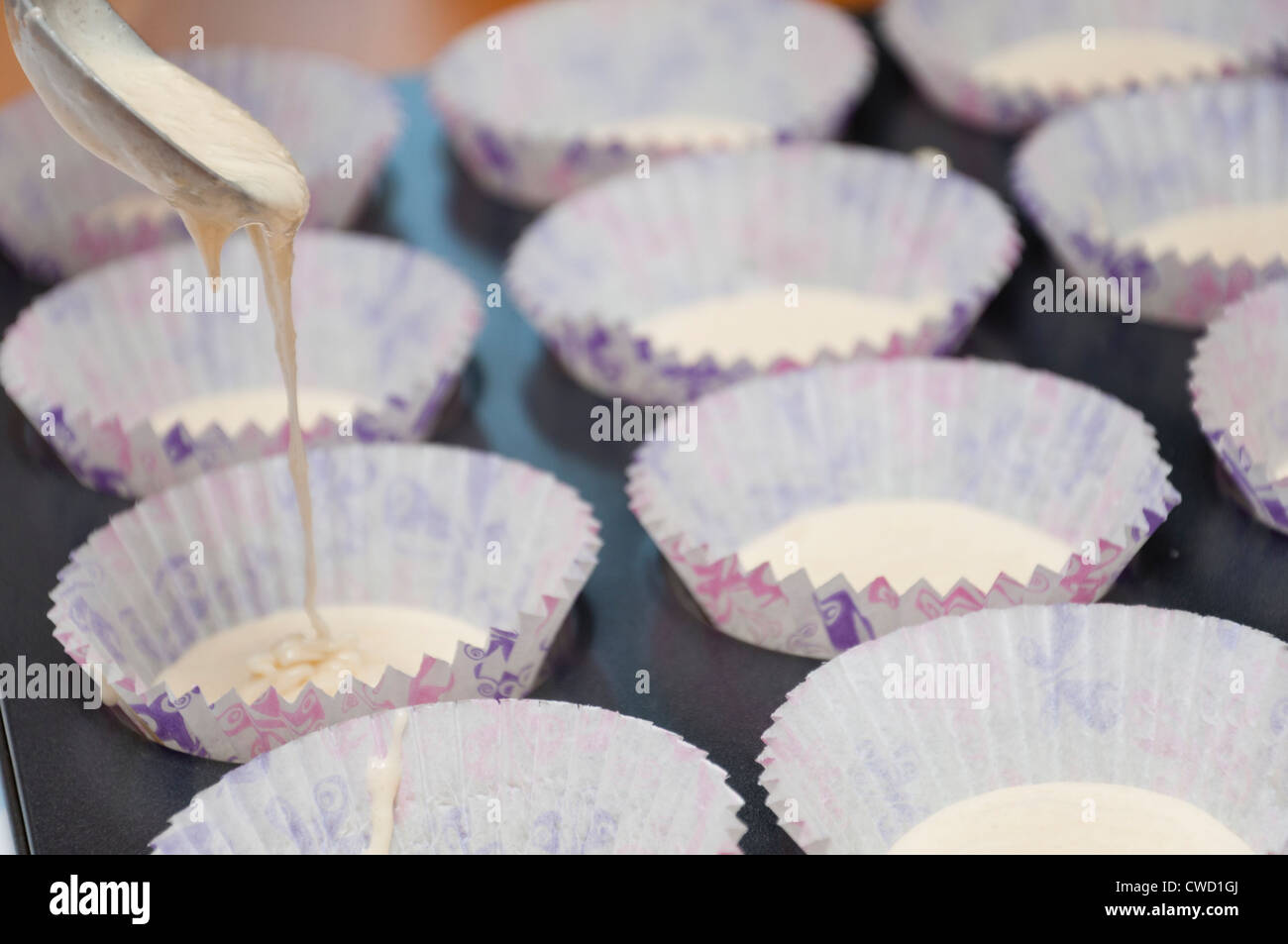 Pouring cake mix into cup cake cases to bake fairy cakes. Stock Photo