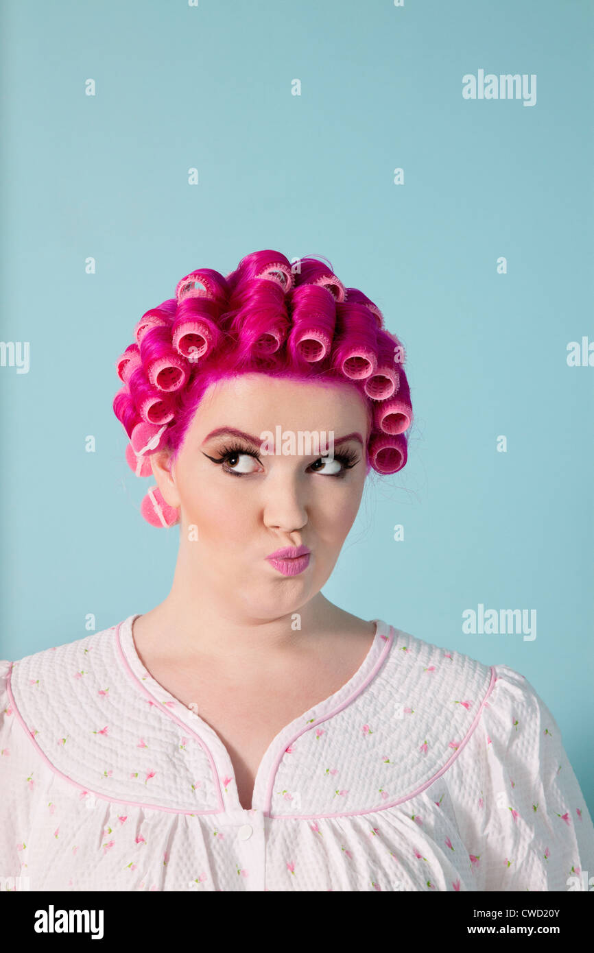 Young woman making faces with pink hair and curlers over colored background Stock Photo