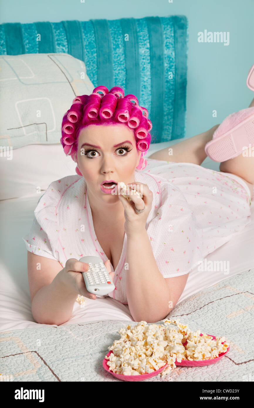 Portrait of shocked young woman watching television with popcorn while lying on bed Stock Photo
