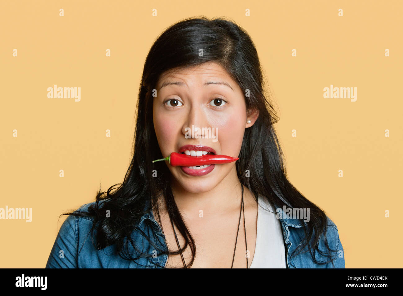 Portrait of a woman with red chili pepper in mouth over colored background Stock Photo