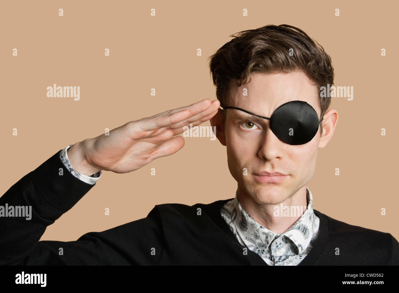 Portrait of a man wearing eye patch saluting over colored background Stock Photo