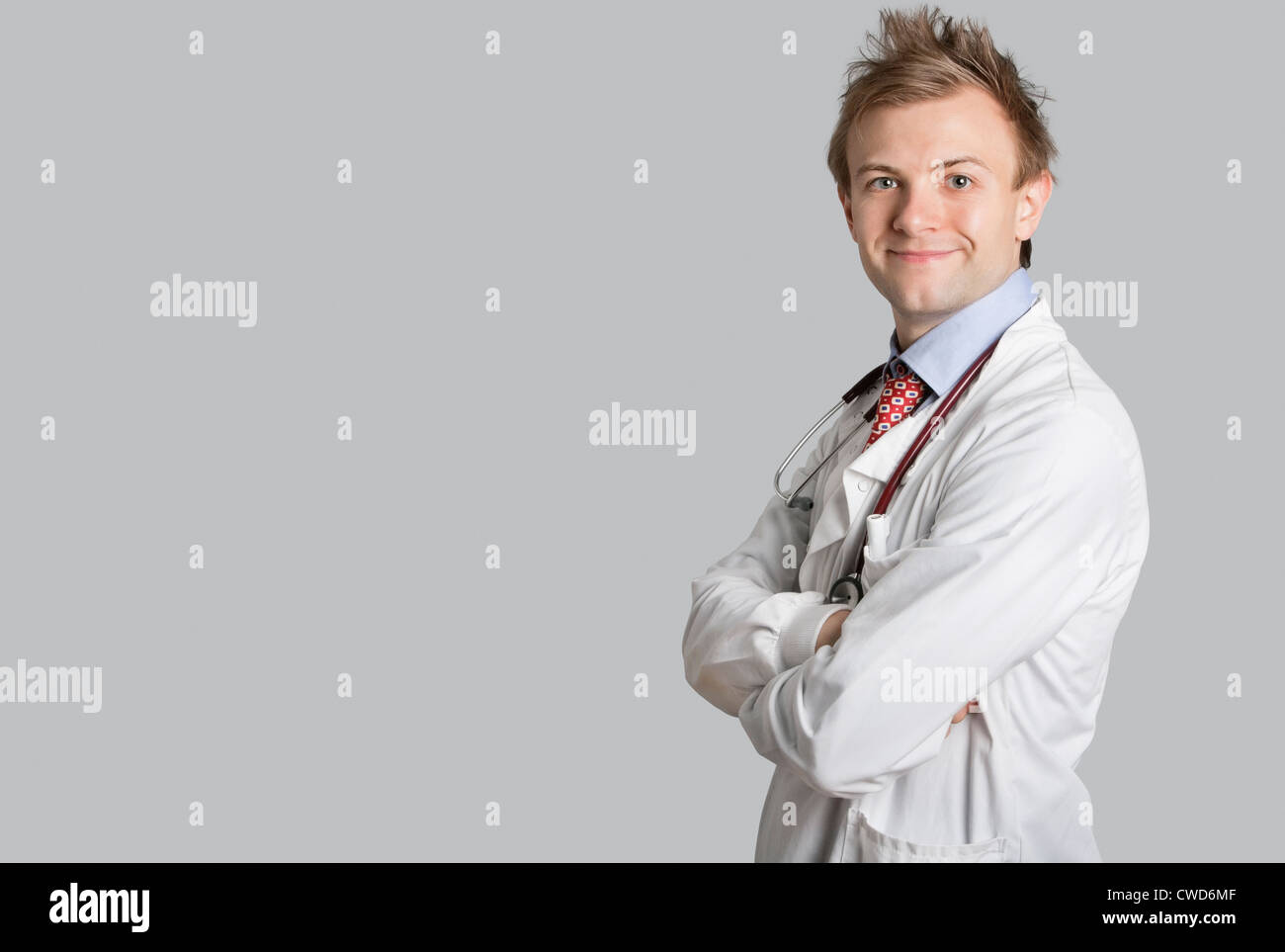 Portrait of a male doctor smiling with arms crossed over gray ...