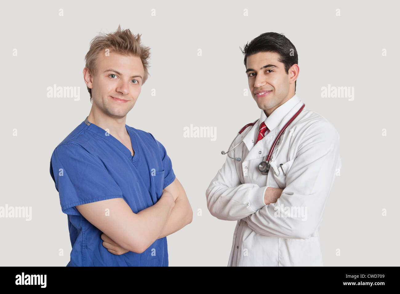 Portrait of happy male nurse and doctor standing with arms crossed over gray background Stock Photo