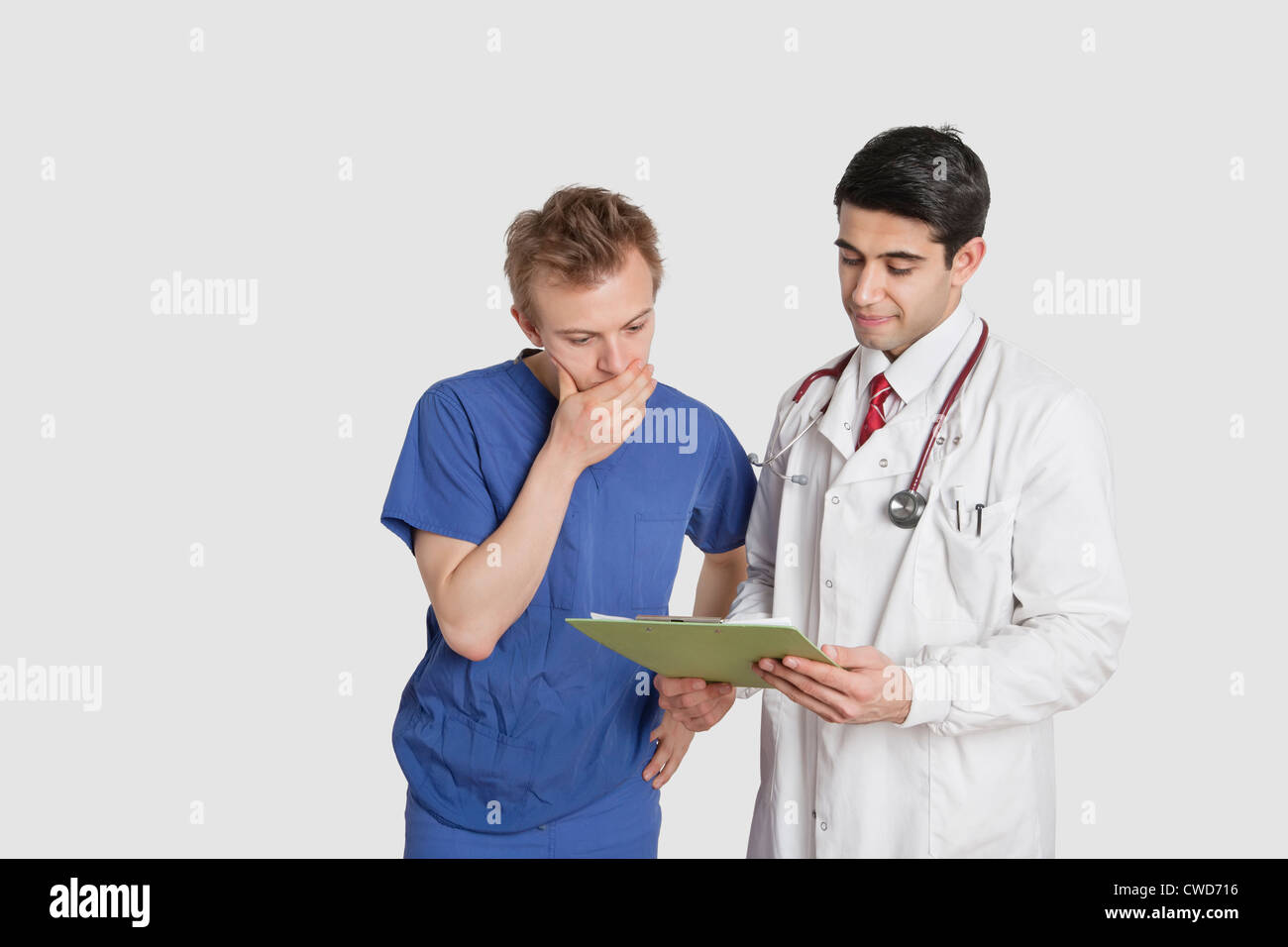 Doctor discussing medical report with male nurse over gray background Stock Photo