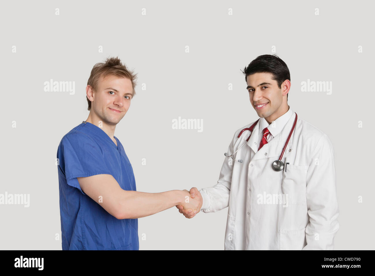 Portrait of doctor and male nurse shaking hands over gray background Stock Photo