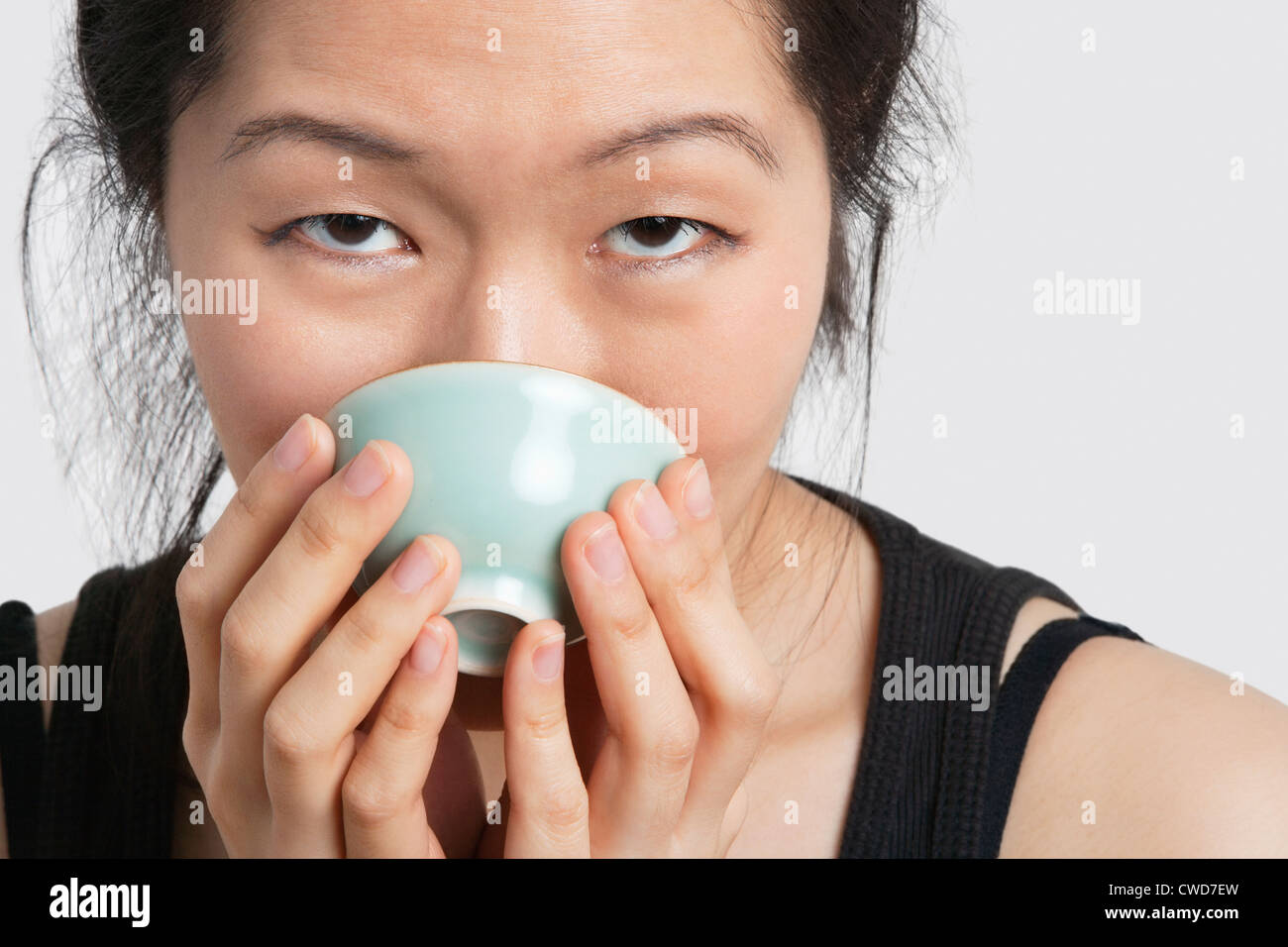 Portrait of a young woman drinking from bowl over light gray background Stock Photo