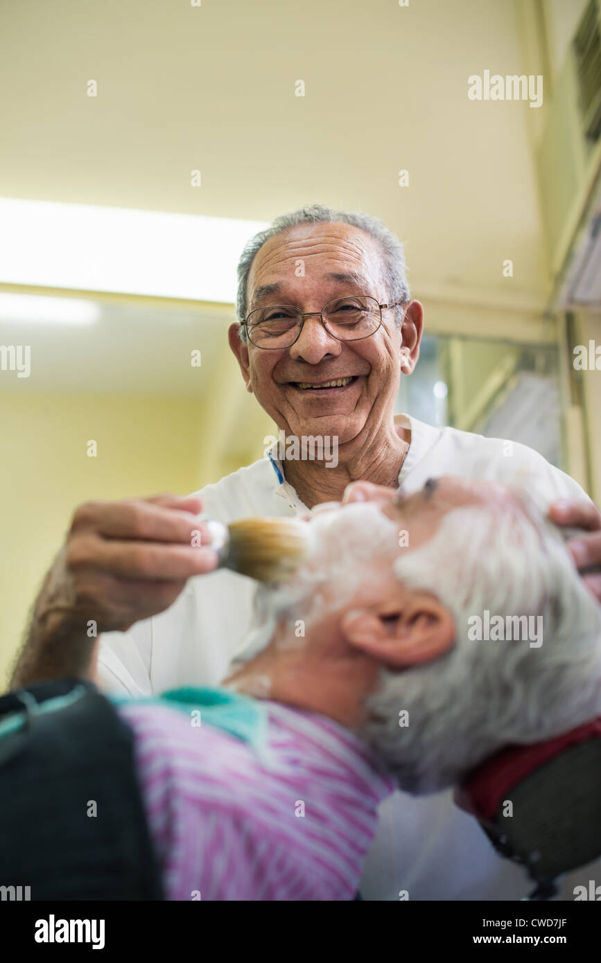 Elderly barber with shave brush applying cream to client in old style