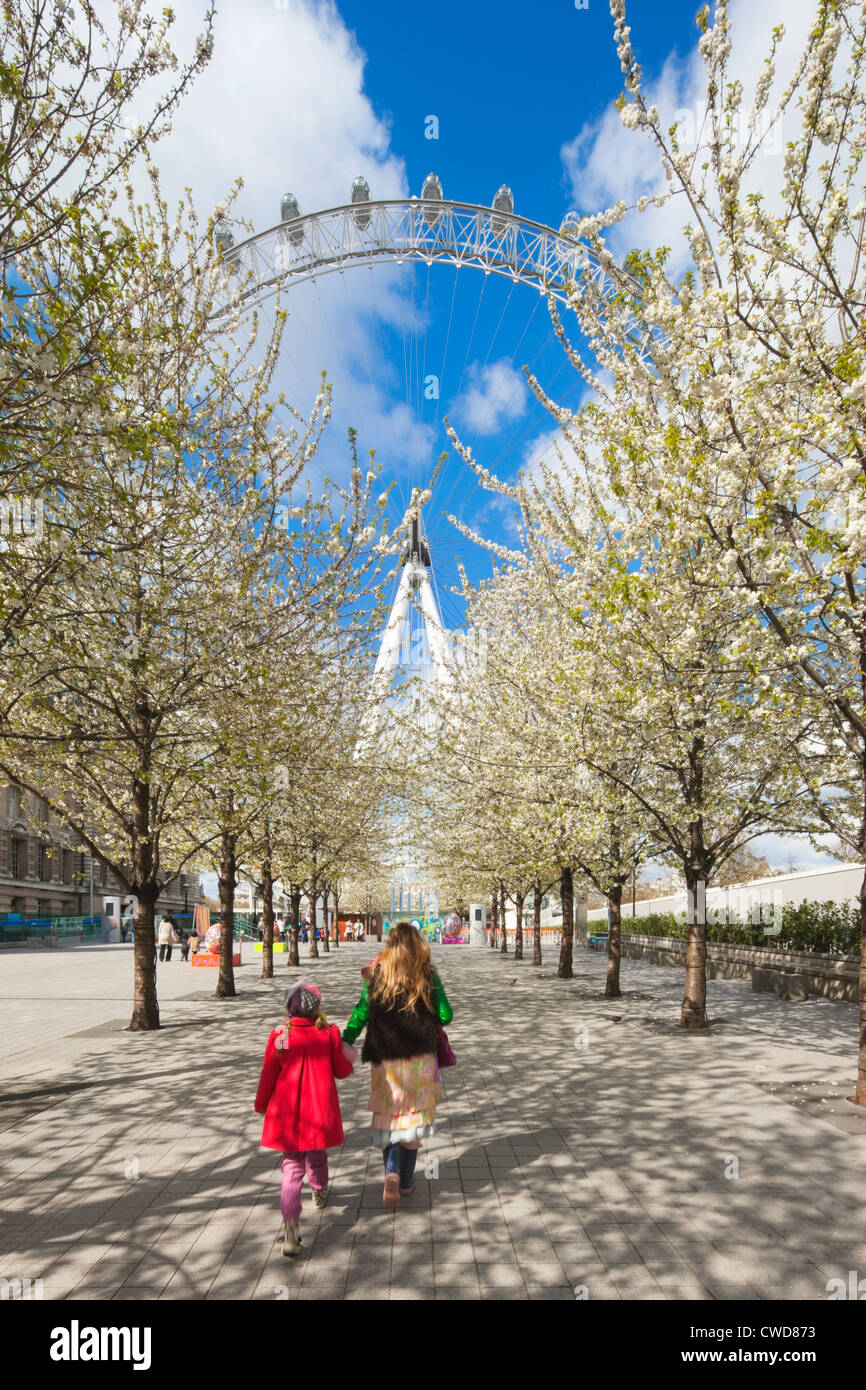 Mother and daughter walking through trees in blossom to the London Eye