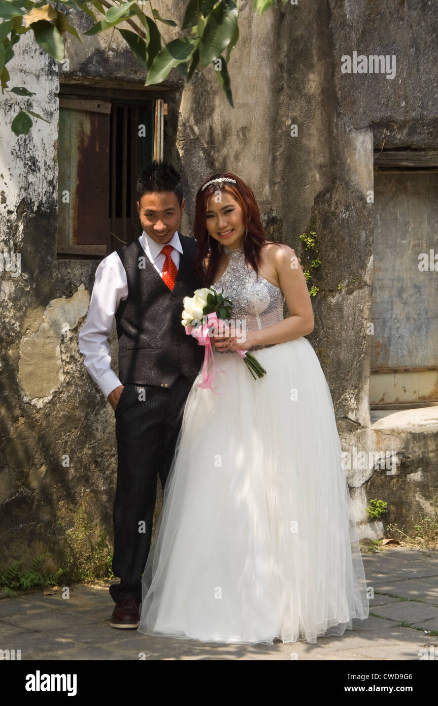 Vertical portrait of a beautiful Vietnamese bride and groom posing for photographs near a derelict building in Vietnam. Stock Photo