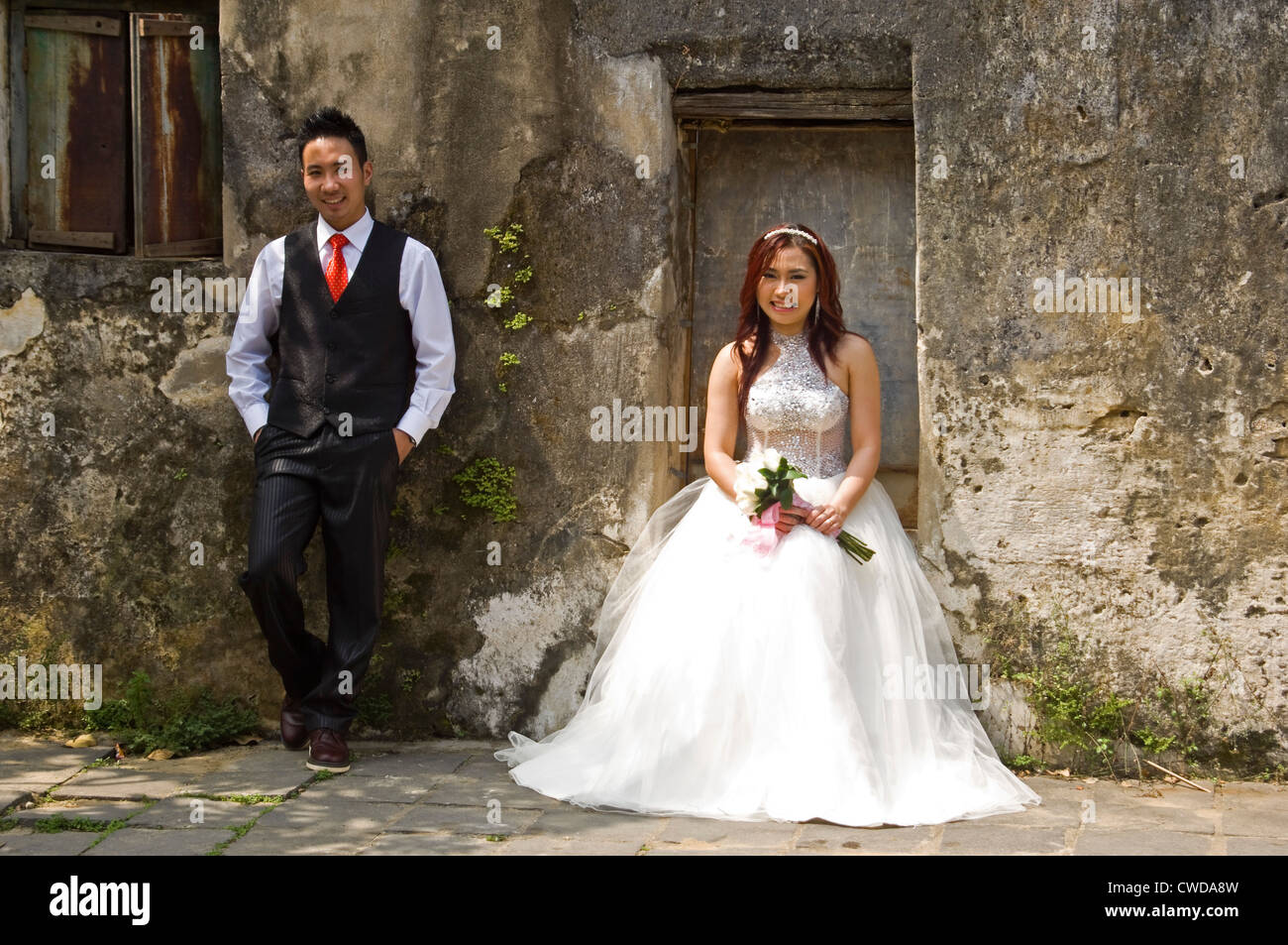 Horizontal portrait of a beautiful Vietnamese bride and handsome groom posing for photographs by a derelict building in Vietnam. Stock Photo