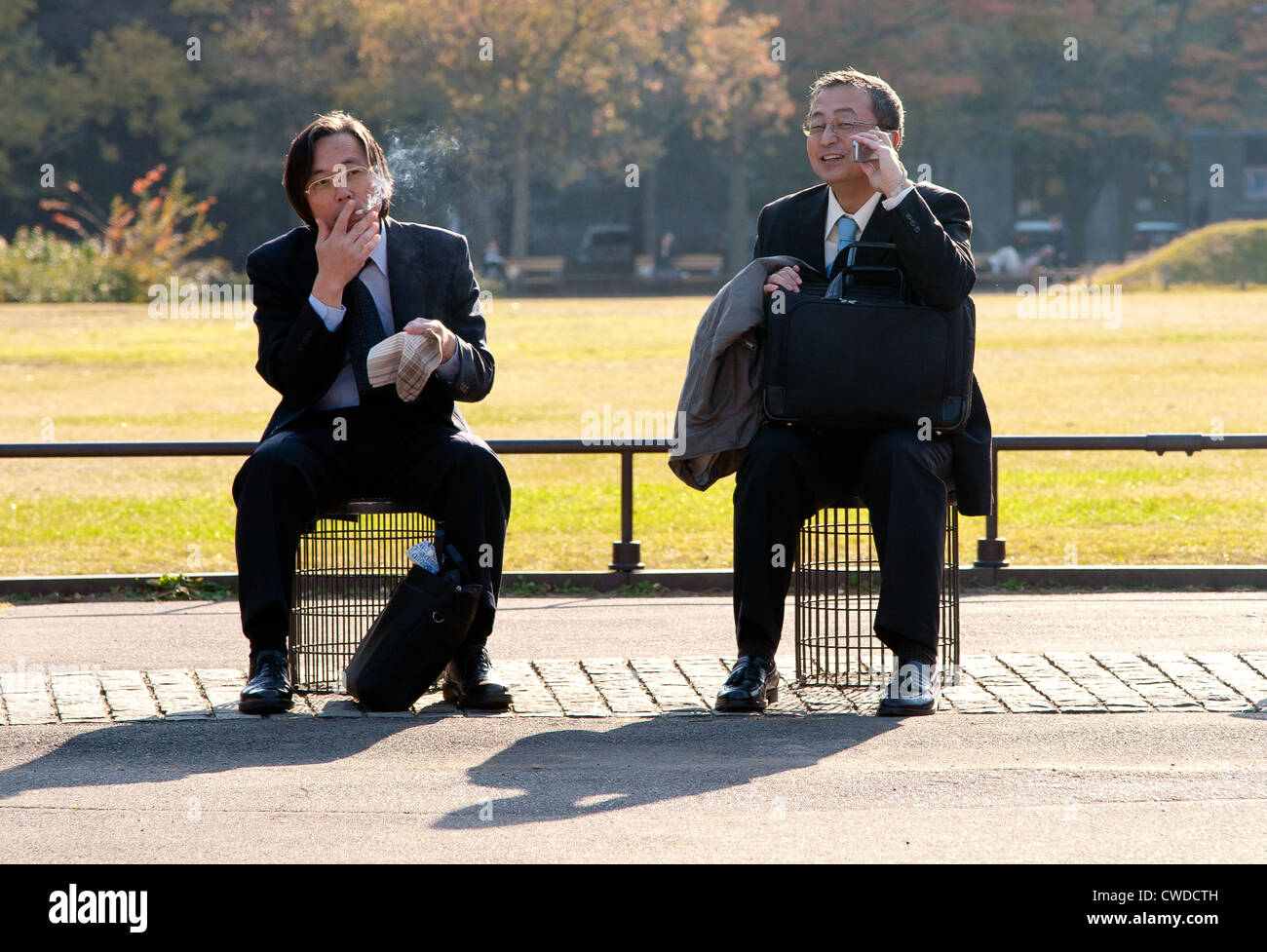 Japanese salarymen resting, smoking and talking on a cellphone in Hibiya Park. Tokyo, Japan. Stock Photo