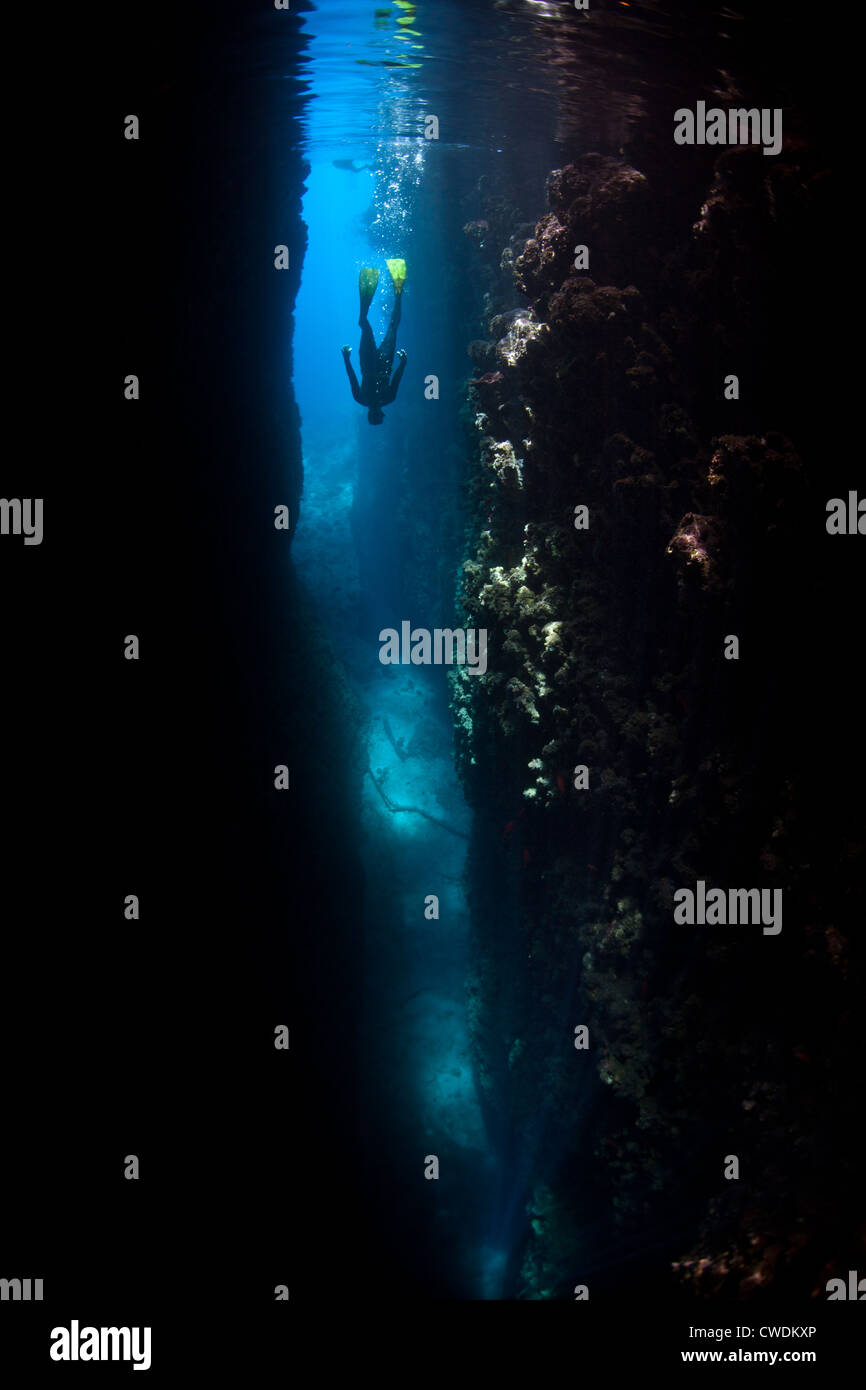 A freediver descends into a deep crevice that cuts into a limestone ...