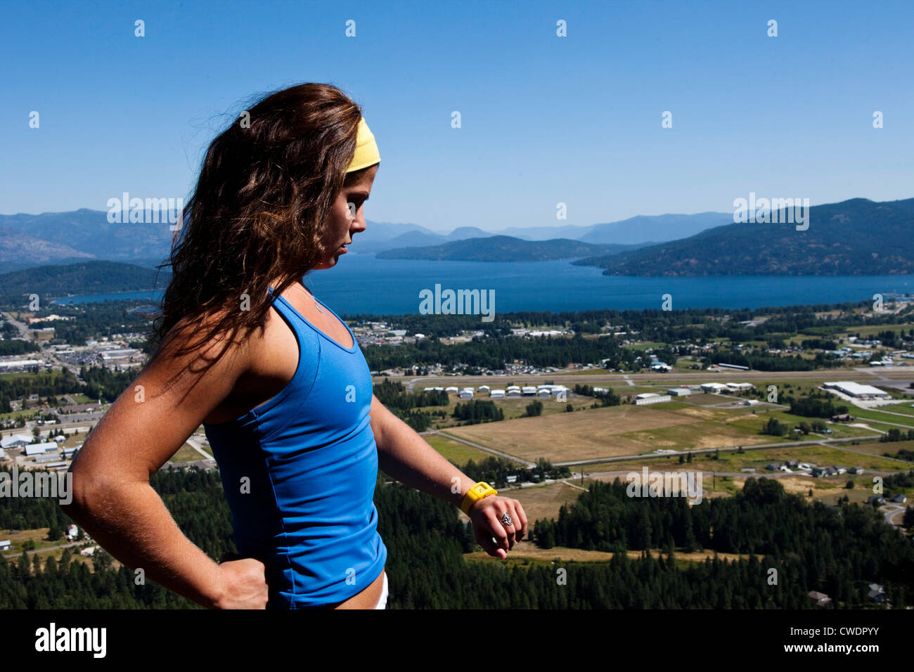 A happy athletic woman hiking stops and looks at her watch overlooking a lake in Idaho. Stock Photo