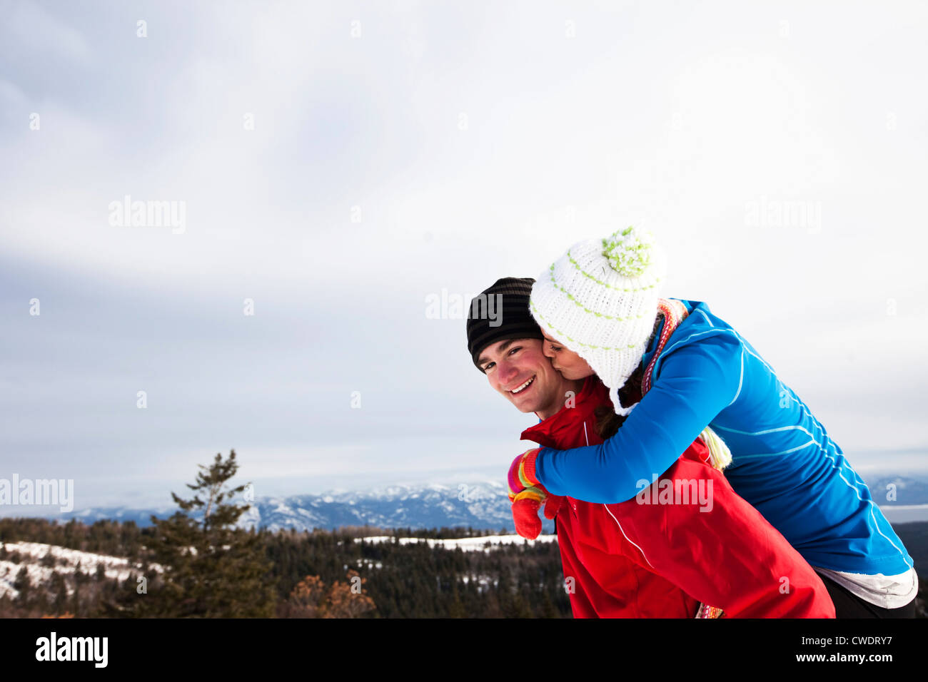 A young adult couple smile and kiss while snowshoeing on a winter day in Idaho. Stock Photo