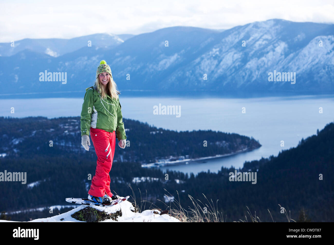 A beautiful young woman smiles while snowshoeing above a lake in Idaho. Stock Photo