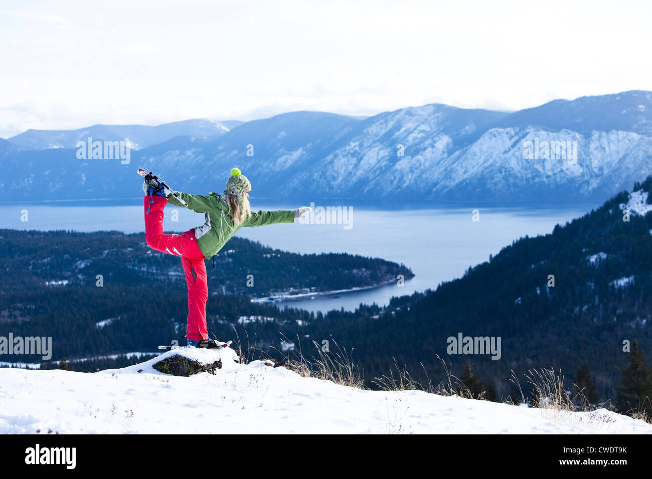 A beautiful young woman doing yoga while snowshoeing above a lake in Idaho. Stock Photo