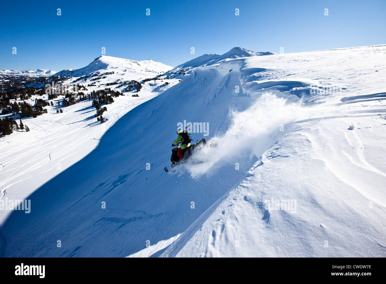 A snowmobiler jumping off a cornice on a sunny winter day in Montana. Stock Photo