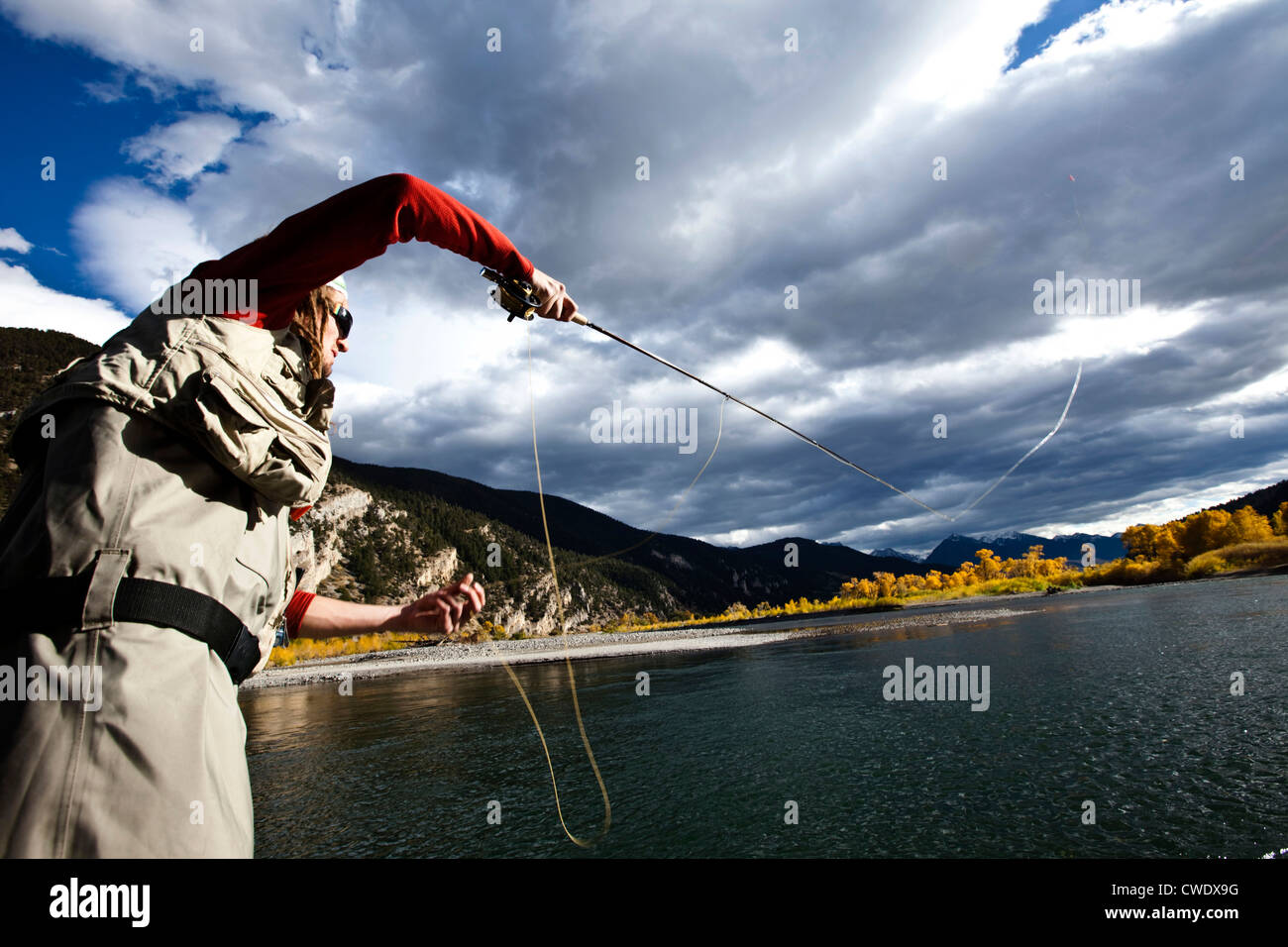 A fly fisher casting his line out of a boat while fly fishing surrounded by fall colors in Montana. Stock Photo