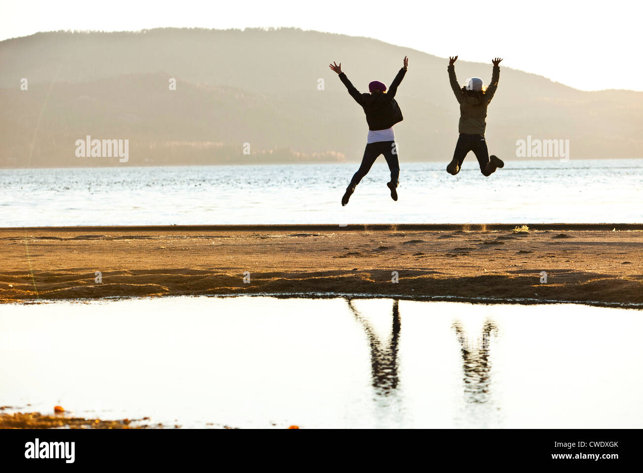 Two athletic women leaping into the air at sunset next to a lake in Idaho. Stock Photo
