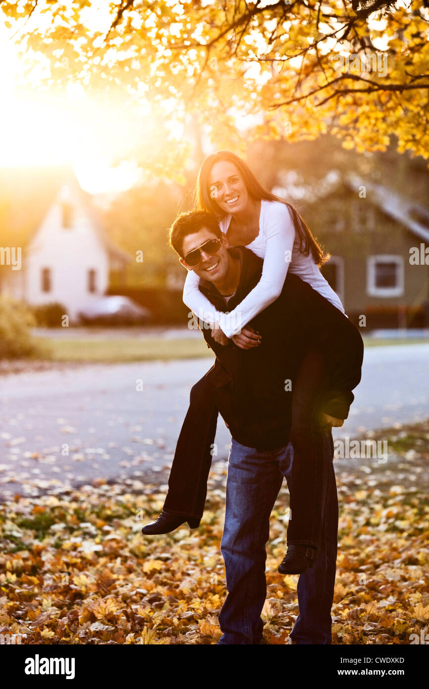 A young adult couple smiling while piggy back riding at sunset surrounded by fall colors in Idaho. Stock Photo
