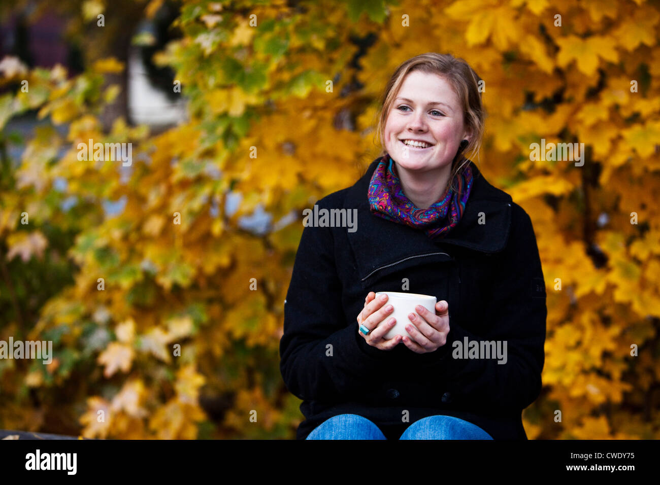 A young woman smiling holds a cup of coffee surrounded by fall colors in Idaho. Stock Photo