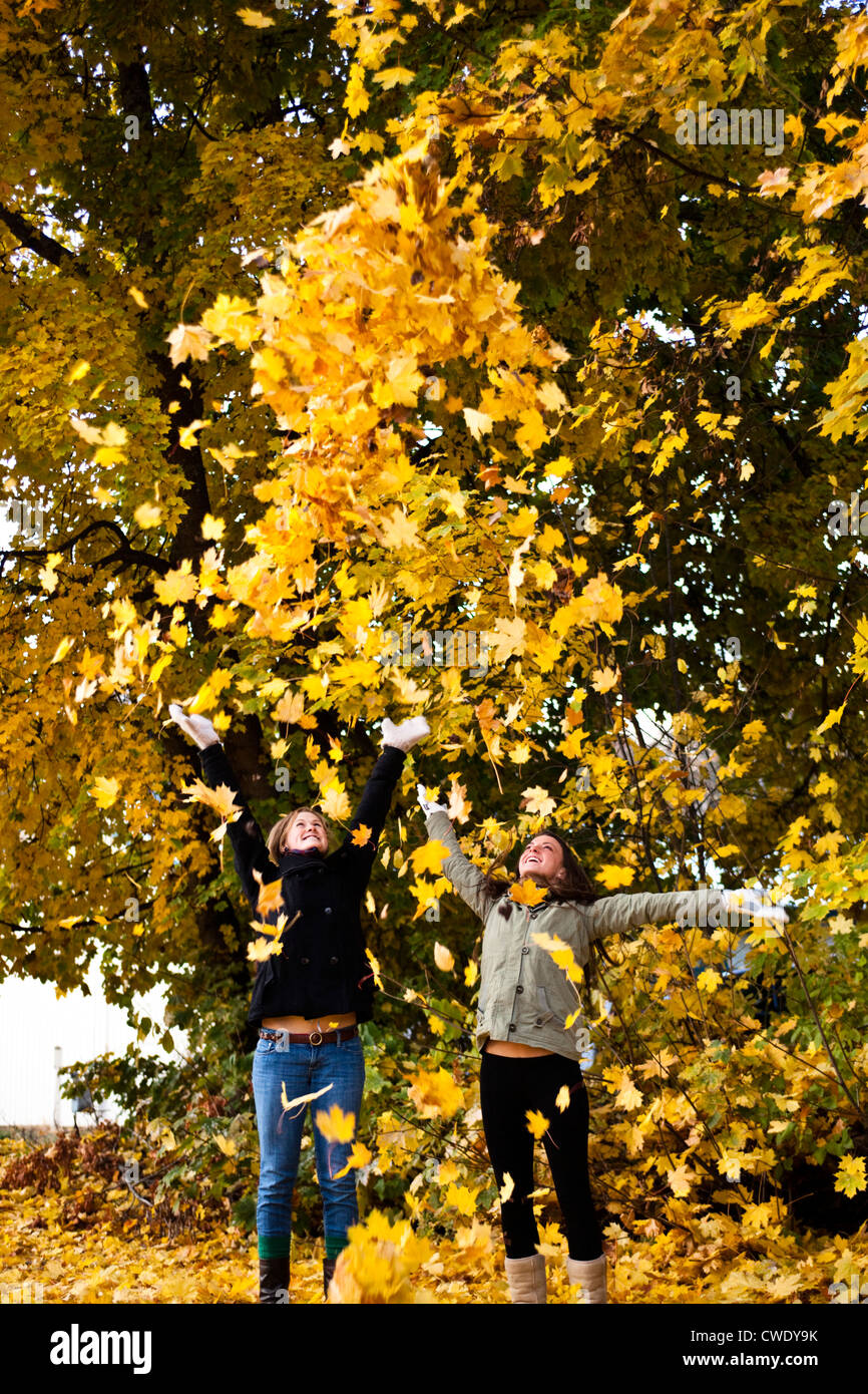 Two young women smiling throw orange leaves into the sky surrounded by fall colors in Idaho. Stock Photo
